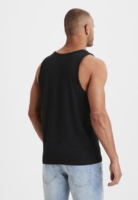 Black tank top with a round neckline and wide armholes, shown from the back. Soft fabric drapes over the shoulders and back.