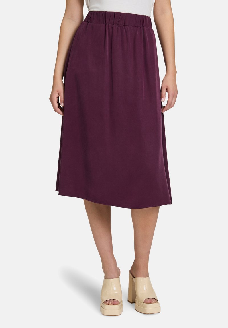 Jupe violette mi-longue avec une taille élastique, en tissu léger. Dotée de poches latérales et d'une texture lisse. Talons compensés beiges présentés.