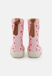 Bottes de pluie en caoutchouc rose avec petits motifs de cœurs rouges, semelles blanches texturées et accents en cuir marron en haut et sur le côté.
