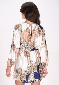 Blumengemustertes Kleid aus weichem Stoff mit langen Ärmeln, einem Schlüsselaugen-Rücken und einer taillierten Taille mit goldenen und marineblauen Akzenten.