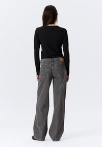 Graue Jeans aus Denim mit weitem Bein, fünf Taschen, sichtbarem Knopfverschluss und einem beigen Lederpatch am hinteren Bund, kombiniert mit einem schwarzen Oberteil.