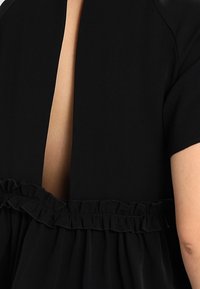 Vestido negro con mangas cortas, un profundo escote en la espalda y un frunido en el cinturón. Textura suave con una silueta fluida.