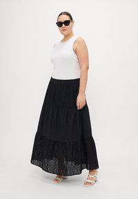 Fustă maxi neagră în bufantă cu detalii perforate la tiv, asortată cu un top alb fără mâneci și sandale albe cu barete. Ochelari de soare negri incluși.