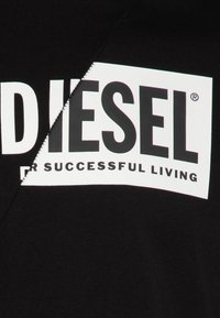 Juoda medvilninė marškinėlių su dideliu baltu stačiakampiu grafiniu elementu, kuriame užrašyta „DIESEL“ ir frazė „FOR SUCCESSFUL LIVING“ storu juodu šriftu.