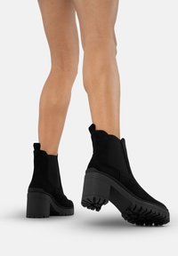 Czarne zamszowe botki za kostkę na masywnym obcasie, z teksturowaną gumową podeszwą, elastycznymi panelami bocznymi i pętelkami do wsuwania.