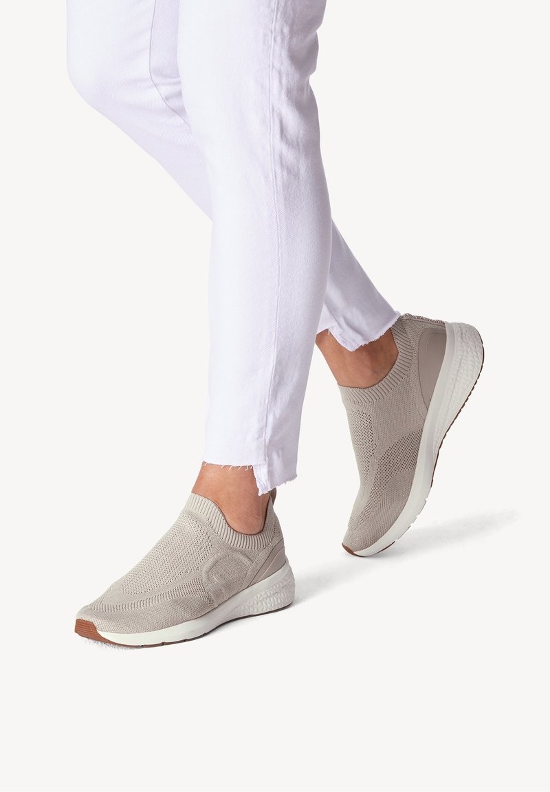 Baskets slip-on beige clair avec un dessus en tricot texturé, semelle blanche et accents en caoutchouc, associées à un denim blanc effiloché.
