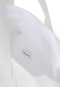 Balta tote maišas, viduje su užtrauktuku kišene, ant kurios yra etiketė su užrašu "OHAPRIL." Lygus paviršius ir paprastas dizainas.