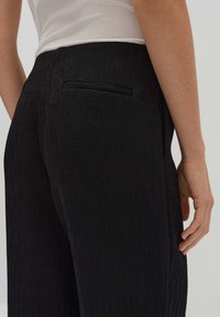 Zwarte corduroy broek met een gestructureerd oppervlak, zichtbare streepjes en een discreet achterzakje. Ontworpen voor een aansluitende silhouette.