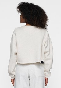 Gekürzter Sweatshirt aus hellem beigen Fleece, mit überschnittenen Schultern und geripptem Rundhalsausschnitt. Verfügt über ein Etikett am hinteren Saum.