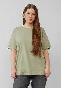 Olijfgroen katoenen T-shirt met korte mouwen, een ontspannen fit en een ronde halslijn, gedragen met donkergrijze jeans. Gladde textuur, geen patronen.
