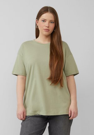 T-shirt en coton vert olive à manches courtes, avec une coupe décontractée et un col rond, porté avec un jean gris foncé. Texture lisse, sans motifs.