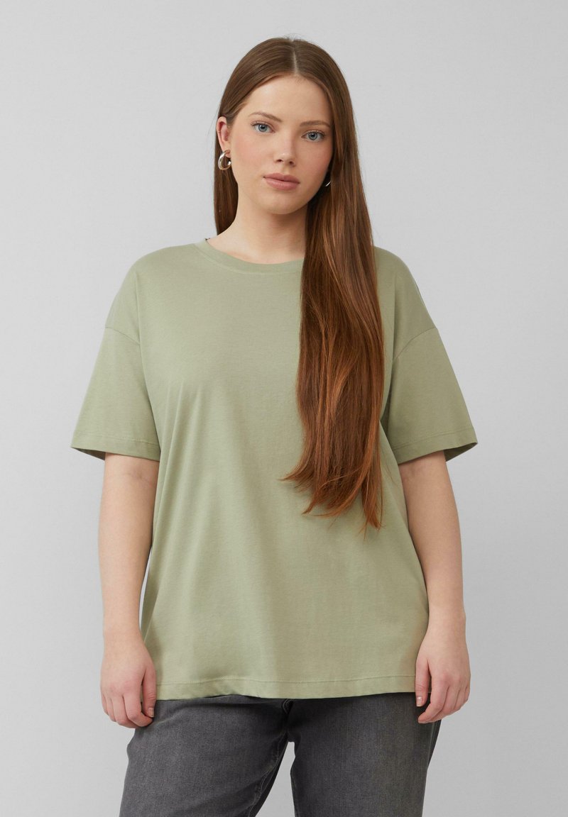 Olijfgroen katoenen T-shirt met korte mouwen, een ontspannen fit en een ronde halslijn, gedragen met donkergrijze jeans. Gladde textuur, geen patronen.