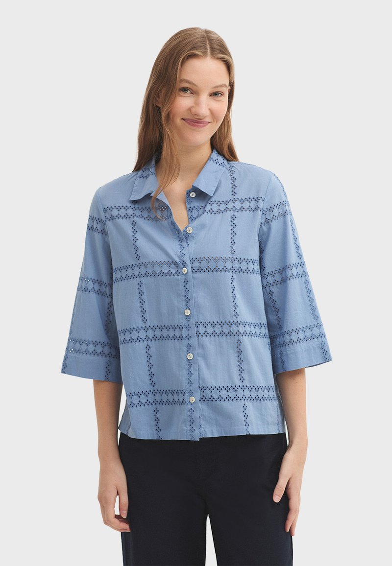 Chemise boutonnée bleu clair avec col, manches trois-quarts et détails en dentelle formant un motif à carreaux. Confectionnée dans un tissu léger.