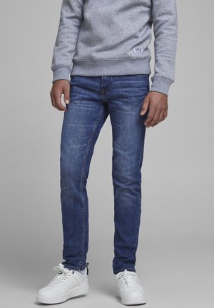 Grijze trui met omgeslagen mouwen, gecombineerd met blauwe spijkerbroek met een slanke pasvorm en vervaagde details. Witte sneakers maken de look compleet.