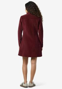Burgundy kordflardress med långa ärmar, rak passform och ryggdetalj. Buren med grå sneakers med kontrasterande ränder.