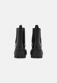 Botas negras hasta el tobillo con un acabado brillante, paneles elásticos en los laterales y una suela gruesa y texturizada. Incluyen dos lengüetas para facilitar el uso.