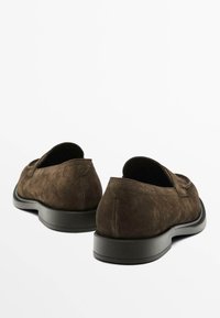 Braune Wildlederschlupfschuhe mit einer niedrigen, schwarzen Gummisohle. Sie zeichnen sich durch eine glatte Textur und ein abgerundetes Fersendesign aus.