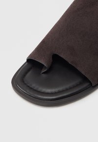 Μαύρο σανδάλι με τετράγωνη μύτη σε σχέδιο slide, με καφέ επάνω μέρος από σουέντ και μικρό εγκοπή κοντά στο άνοιγμα της μύτης.