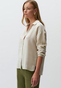 Crème linnen overhemd met kraag, opgerolde mouwen en een relaxed fit, gecombineerd met groene op maat gemaakte broek. Zachte textuur en lichte hang.