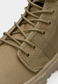 Μπεζ καμβαδένιο παπούτσι υψηλής τομής με υφή στην επιφάνεια, στρογγυλά κορδόνια, μεταλλικά κορδονότρυπα και λαστιχένια εξωτερική σόλα με ανθεκτικό σχέδιο.