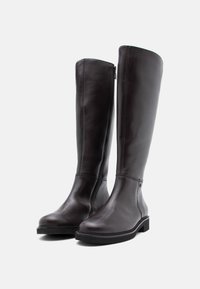 Botas de cuero marrón hasta la rodilla con una textura suave, puntera redonda y cremallera lateral. Presentan un tacón bajo y detalles de costura sutiles.