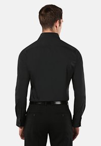 Zwarte overhemd met een klassieke kraag, lange mouwen en knoopmanchetten. Gladde textuur en getailleerde pasvorm. Draagt met een zwarte broek.
