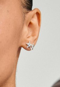 Los pendientes en forma de estrella plateada se muestran en la oreja de un modelo, presentando una superficie suave y brillante y un diseño sencillo.