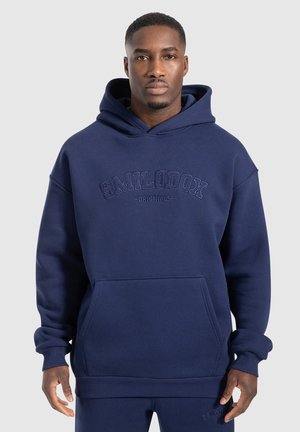 Navy blå hættetrøje lavet af blødt stof, som har en frontkangaroo-lomme, ribbede manchetter og præget "SMILODOX ORIGINALS" tekst.