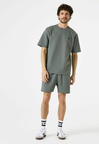 Grijze shirt met wafelstructuur en korte mouwen, met bijpassende shorts. Het shirt heeft een ronde halslijn en een klein logo; de shorts hebben een elastische tailleband.