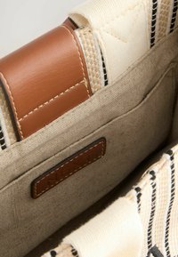 Tan leren accenten op een crèmekleurige en gemusterde stoffen tasinterieur met een klein zakje, voorzien van een zichtbaar merkembleem.