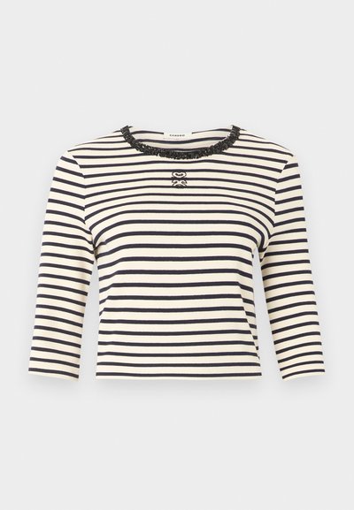 Λευκό και μαύρο μακρυμάνικο τοπ με οριζόντιες ρίγες, λαιμόκοψη σε στρογγυλό σχήμα διακοσμημένη με παγιέτες και μικρό διακοσμητικό λογότυπο στο κέντρο του στήθους.