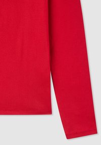 Camicia a maniche lunghe rosso brillante con cuciture visibili sul tessuto di cotone, posizionata su uno sfondo grigio chiaro.