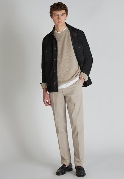 Giacca di velluto a coste nera sopra un maglione di maglia beige, abbinata a pantaloni chino crema e mocassini neri. Design semplice e minimale.