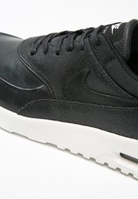 Svart läder- och textilsneakers med rund tå, tonad sömnad och vit sula. Har Nike-logotyp på tungan och texturerade detaljer.