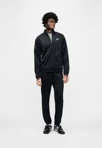 Μαύρη φόρμα Nike με επάνω μέρος με φερμουάρ και παντελόνι που ταιριάζει · διαθέτει κομψό σχεδιασμό, εφαρμοστά μανσέτες και λογότυπο στο στήθος και στο πόδι του παντελονιού.