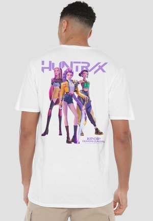 Mann trägt weißes T-Shirt mit drei animierten weiblichen Charakteren in futuristischen Outfits und mit Schwert, Text "HUNTRX" und "K-POP DEMON HUNTERS".