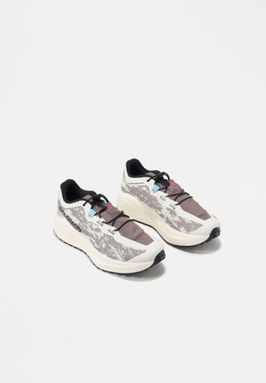 Par de zapatillas deportivas blancas y grises con un patrón, cordones negros y suelas acolchadas sobre un fondo blanco.