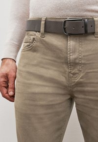 Pantaloni in cotone beige con una texture liscia, dotati di tasche laterali e una cintura in ecopelle grigia con una fibbia nera rettangolare.