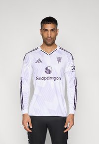 Camisola de futebol branca de manga comprida com detalhes em roxo e padrões geométricos. Apresenta o logótipo da Adidas e a marca "Snapdragon" na frente.