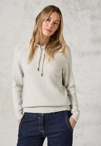 Lichtgrijze gebreide sweatshirt met geribbelde textuur, verstelbare trekkoordkap en lange mouwen. Gepaard met donkerblauwe jeans.