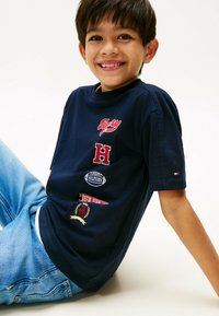 Camiseta de algodón azul marino de manga corta, con logotipos bordados: "Tommy", "H", un balón de rugby y "Nueva York", así como un pequeño logo en la manga.