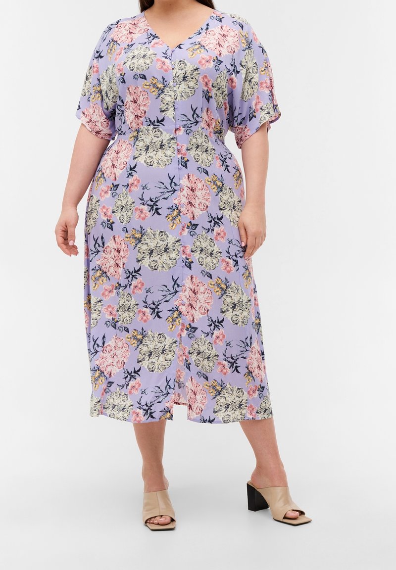 Blommig midiklänning i ljuslila tyg; har korta ärmar, knappstängning och blandade blommor i rosa, gult och marinblå nyanser.