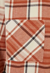 Flanelová košile s červenobíločerným kostkovaným vzorem a kontrastní kostičkovanou kapsou. Měkká, strukturovaná tkanina.