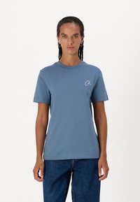 Camiseta de manga corta y cuello redondo en una suave tela azul con un sutil logo blanco "CK" en el pecho. Diseño ajustado con una textura suave.