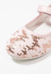 Płaskie buty baletowe w kolorze różowego złota i białych cekinów z różową metaliczną paskiem. Okrąły nosek, gładka tekstura i płaska podeszwa. Szczegółowy wzór z cekinów.