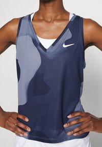 Nike ärmlös tröja i marinblått och grått med ett texturerat, andande material, V-ringning och logotyp på vänster bröst.