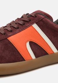 Marin mockasiner i mocka med orange skinnaccent, vita detaljer och bruna snören. Gummisulans färg är ljusbrun och har en texturerad yta.