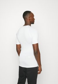 Camiseta de compresión de manga corta blanca con una textura suave, diseño ajustado y un detalle de logo en el cuello y la parte baja de la espalda.