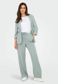 Light green, linen blend suit featuring a relaxed blazer with rolled sleeves and drawstring pants, paired with a white top and white sneakers.