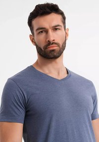 Tmavě modré tričko s výstřihem do V vyrobené z měkké látky. Krátké rukávy, úzký střih s hladkou strukturou a bez viditelných vzorů či ozdob.